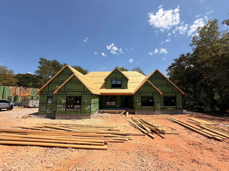 A new house framed and sheathed on red Arkansas clay, lumber stacked out front, before the wiring and the drywall go in