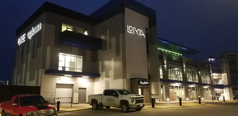 A lettered Craine's work pickup at the curb of a three-storey commercial building, lit up at night